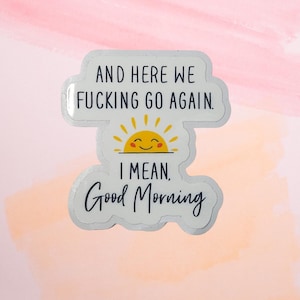 May include: A white sticker with the text "AND HERE WE FUCKING GO AGAIN." and "I MEAN. Good Morning" in black font. A yellow smiling sun graphic is between the phrases. The sticker is on a pink and peach watercolor background.