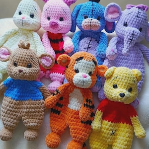 May include: A collection of seven handmade crochet plush toys featuring various animal characters. The group includes a cream rabbit, a pink pig, a blue donkey, a purple elephant, a brown bear, an orange tiger, and a yellow bear, all with black eyes.