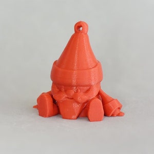 May include: A 3D-printed, orange gnome ornament. The gnome has a pointed hat, a long beard, and is sitting with its legs outstretched. It has a loop at the top for hanging. The ornament is made of plastic.