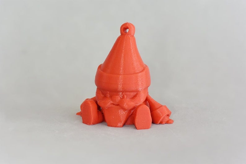 May include: A 3D-printed, orange gnome ornament. The gnome has a pointed hat, a long beard, and is sitting with its legs outstretched. It has a loop at the top for hanging. The ornament is made of plastic.