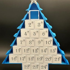 May include: A blue and white Christmas tree advent calendar with 24 numbered doors. The tree is made of wood and has a star on top.