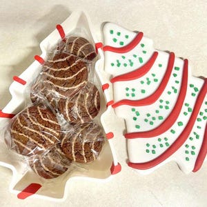 May include: A Christmas tree-shaped serving dish with a lid, filled with individually wrapped chocolate cookies. The lid is decorated with red and green accents. The cookies have a brown and white striped pattern.