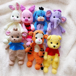Può includere: Una collezione di animali di peluche all'uncinetto fatti a mano in vari colori. I personaggi includono un coniglietto bianco, un maialino rosa, un asino blu, un elefante viola, un orso marrone, una tigre arancione e un orso giallo. Ogni giocattolo è alto circa 15 cm.
