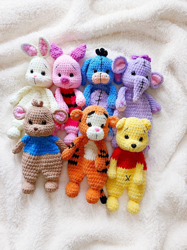 May include: A collection of seven handmade crochet plush toys featuring various animal characters. The set includes a white rabbit, a pink pig, a blue donkey, a purple elephant, a brown bear in a blue shirt, an orange tiger, and a yellow bear in a red shirt.
