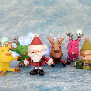 May include: A collection of colorful Christmas ornaments featuring Santa Claus, reindeer, and an elf. The ornaments are in various colors, including red, green, yellow, and pink. The Santa ornament has a white beard and a red hat. The reindeer have antlers.