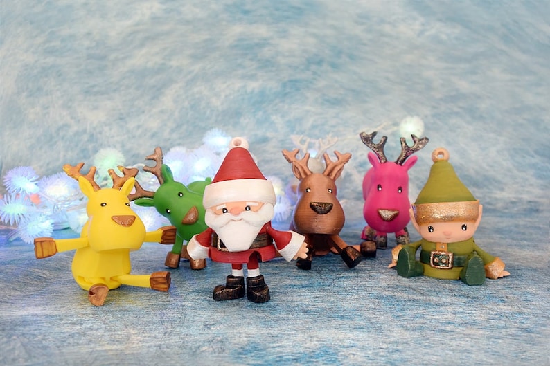 May include: A collection of colorful Christmas ornaments featuring Santa Claus, reindeer, and an elf. The ornaments are in various colors, including red, green, yellow, and pink. The Santa ornament has a white beard and a red hat. The reindeer have antlers.