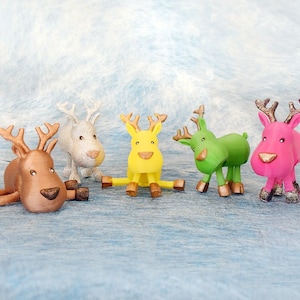 May include: Five colorful reindeer figurines in brown, white, yellow, green, and pink. Each has antlers and a nose in a contrasting color. The reindeer are posed in various positions, some standing and one lying down.