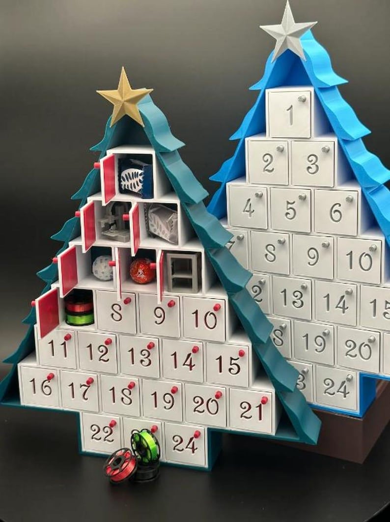 May include: Two white Christmas tree advent calendars with blue and green accents. The calendars have numbered doors with red and silver accents. The doors are open on the left calendar, revealing small gifts inside.