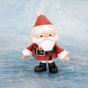May include: A small Santa Claus figurine with a red suit, white beard, and a matching hat. The figure has a black belt with a gold buckle and black boots. The background is a light blue, textured surface.