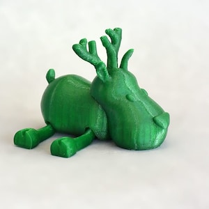 May include: A green, 3D-printed toy deer figurine. The deer is lying down with its legs extended and has antlers. The toy is a solid green color and appears to be made of plastic. The background is plain white.