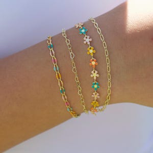 May include: Four gold-colored bracelets. One bracelet features colorful, oval-shaped links. Another has a delicate heart-shaped chain. The third has small, colorful flower charms. The last bracelet has a simple chain design.