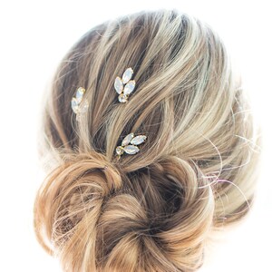 May include: Three gold hair clips with clear crystal accents. The clips are arranged in a row on a woman's hair.