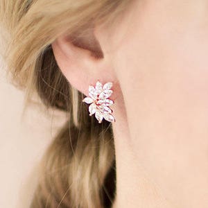 May include: Rose gold earrings with a cluster of clear cubic zirconia stones in a floral design.
