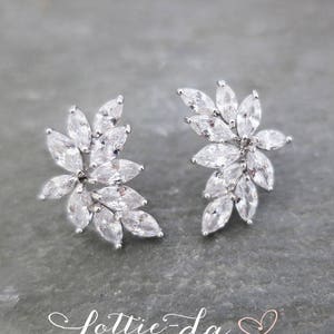 May include: A pair of silver earrings with a floral design featuring clear cubic zirconia stones.