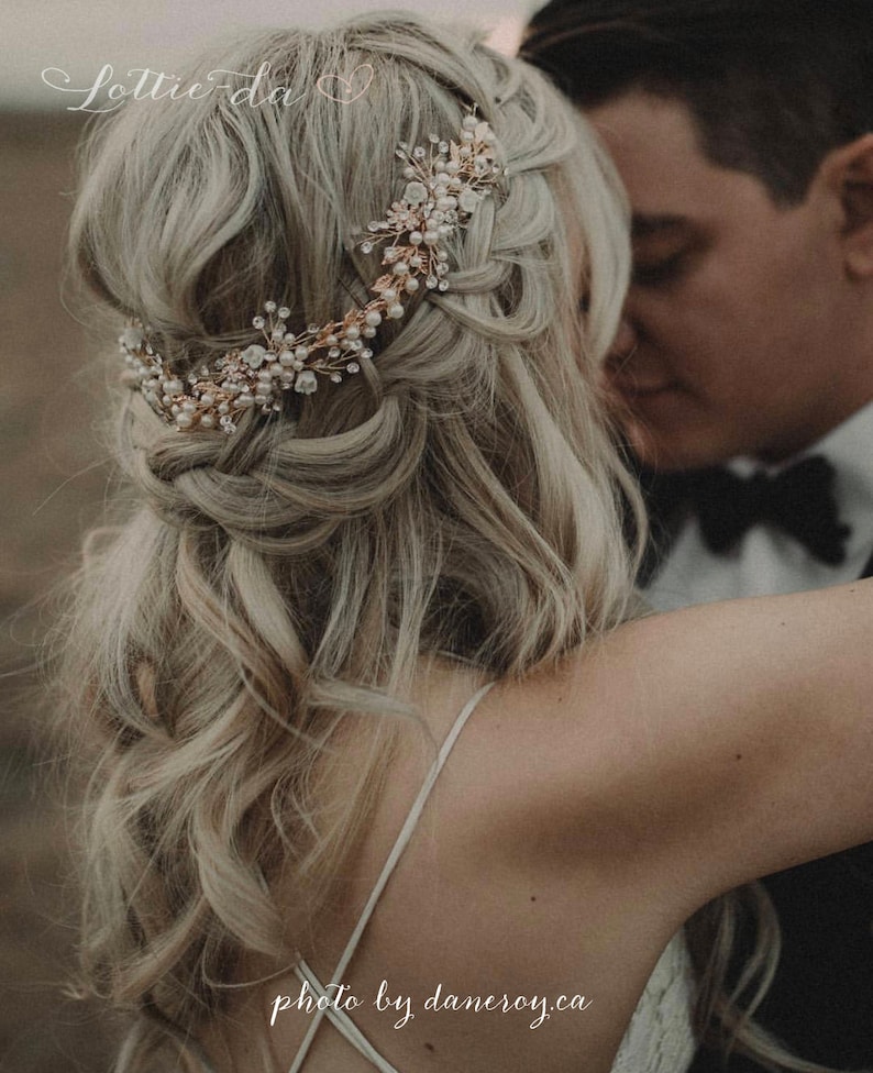 Pu&ograve; includere: Una sposa con lunghi capelli biondi che indossa un delicato pettine per capelli in oro e perle. Il pettine presenta un design floreale con piccole perle e cristalli. La sposa indossa un abito bianco e guarda lo sposo.