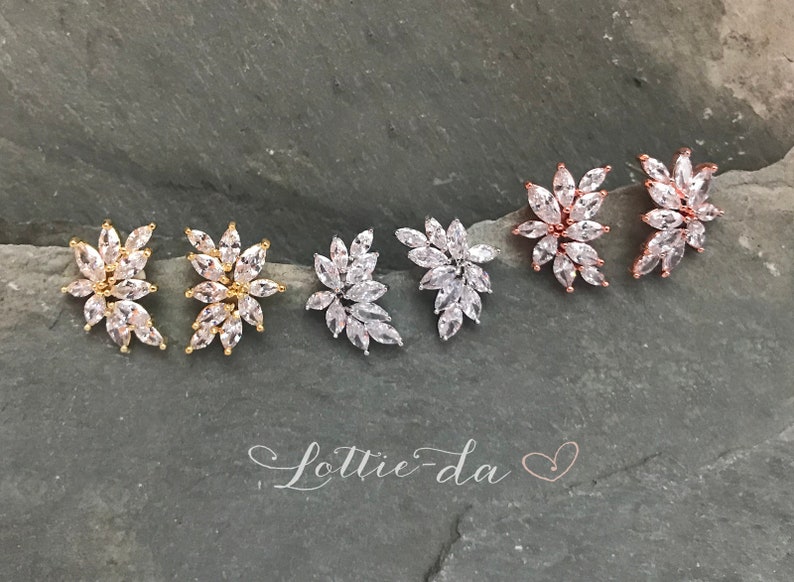 May include: Four pairs of earrings with a floral design. The earrings are made of gold, silver, and rose gold. Each earring features a cluster of clear cubic zirconia stones.