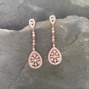 Pu&ograve; includere: Un paio di orecchini pendenti in oro rosa a forma di goccia. Gli orecchini sono adornati con pietre di zircone cubico trasparenti.