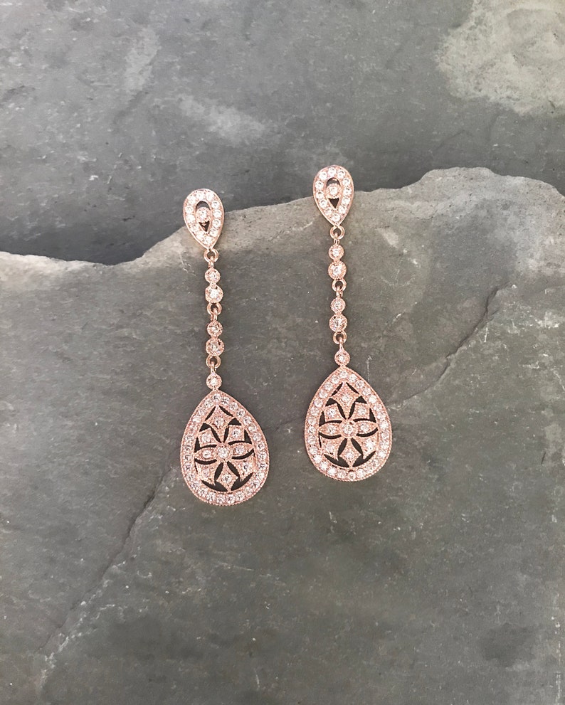 Pu&ograve; includere: Un paio di orecchini pendenti in oro rosa a forma di goccia. Gli orecchini sono adornati con pietre di zircone cubico trasparenti.