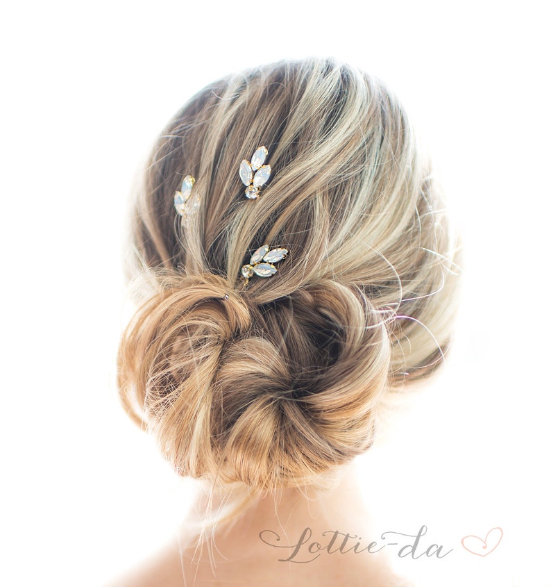 May include: Three gold hair clips with clear crystal accents. The clips are arranged in a row on a woman's hair.