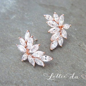 May include: Rose gold earrings with a floral design featuring clear cubic zirconia stones.