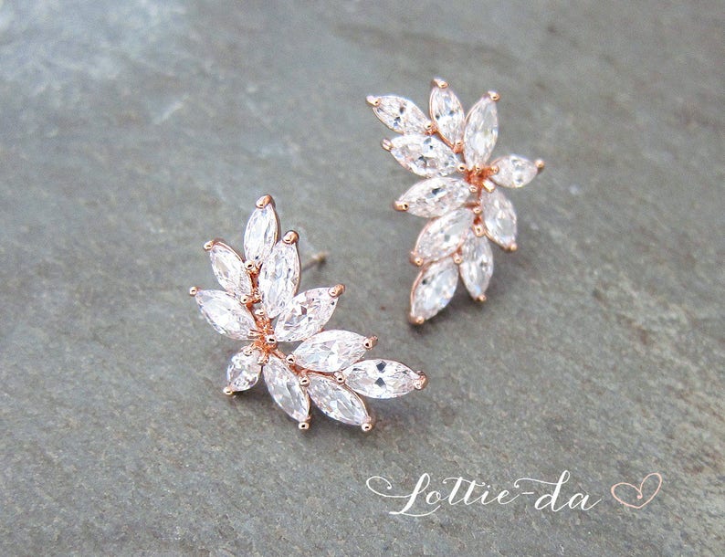 May include: Rose gold earrings with a floral design featuring clear cubic zirconia stones.
