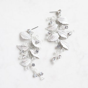 May include: A pair of silver earrings with a leaf design and clear crystals.