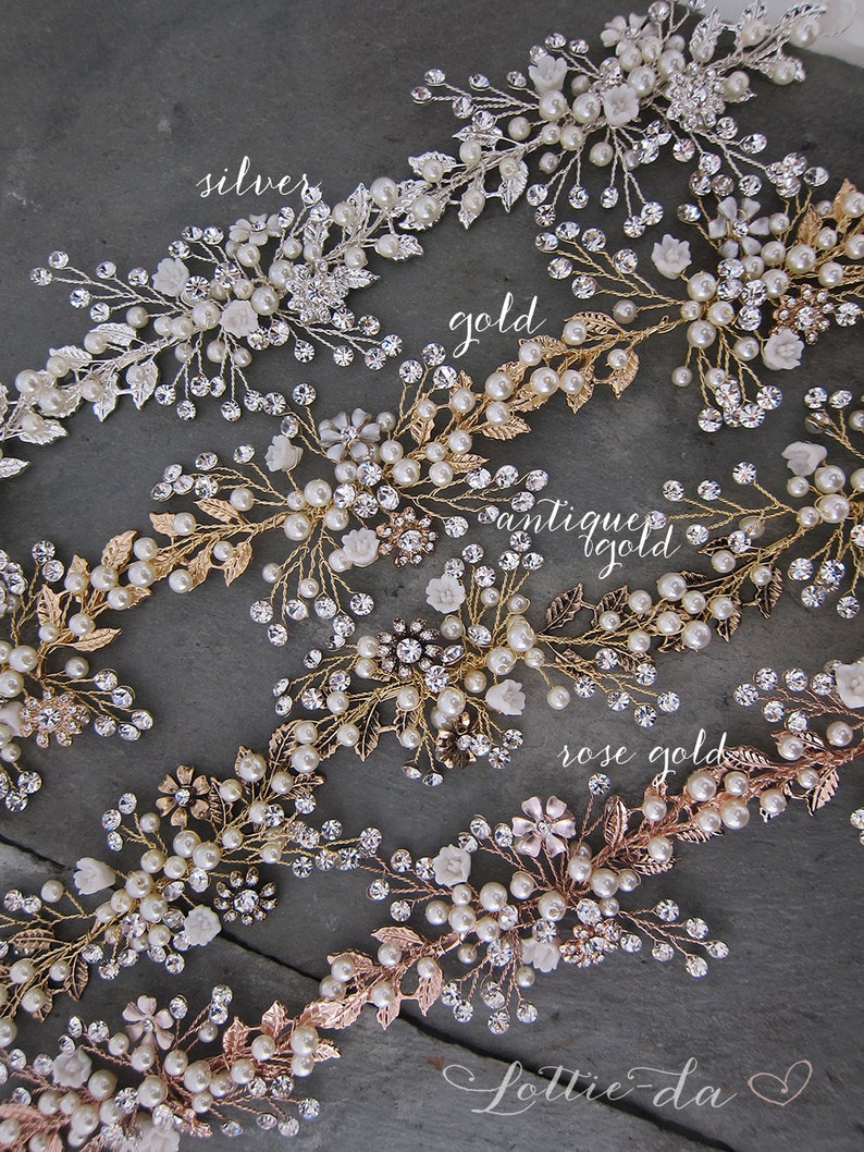 Pu&ograve; includere: Cinque pettini per capelli con decorazioni di perle e cristalli in finiture argento, oro, oro antico e oro rosa. I pettini sono disposti in fila su uno sfondo grigio.