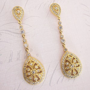 Pu&ograve; includere: Un paio di orecchini pendenti in oro con un design a forma di lacrima. Gli orecchini sono adornati con pietre di zircone cubico trasparenti.