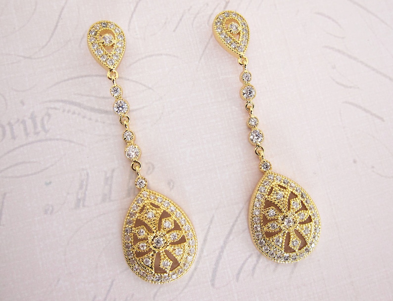 Pu&ograve; includere: Un paio di orecchini pendenti in oro con un design a forma di lacrima. Gli orecchini sono adornati con pietre di zircone cubico trasparenti.