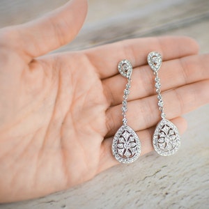 Pu&ograve; includere: Un paio di orecchini a goccia d'argento con un design floreale e cristalli trasparenti.