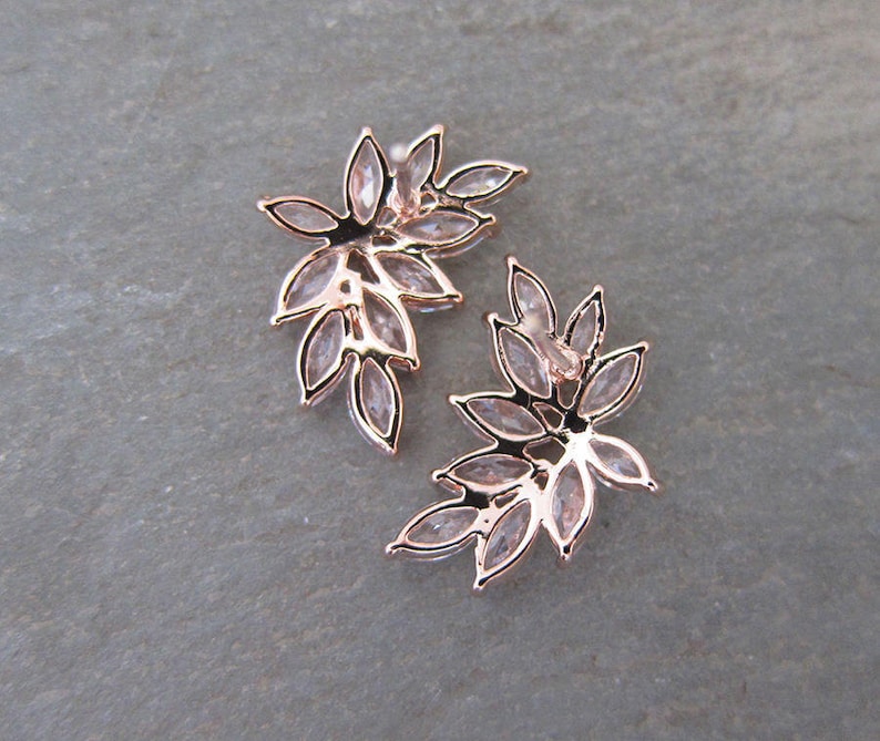 May include: A pair of rose gold earrings with a leaf design. The earrings are made of metal and have clear crystals.