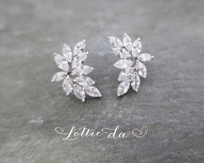 May include: A pair of silver earrings with a floral design featuring clear cubic zirconia stones.