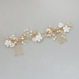 May include: Gold hair comb with white flowers and pearls. The comb has a delicate floral design with leaves and small pearls.