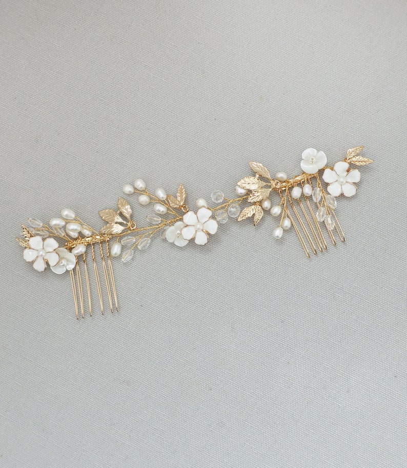 May include: Gold hair comb with white flowers and pearls. The comb has a delicate floral design with leaves and small pearls.