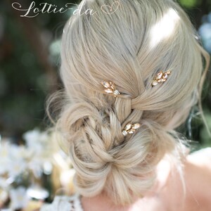 May include: A woman with blonde hair wearing a white dress with a lace pattern. Her hair is styled in a bun with three gold hair pins with clear rhinestones. The hair pins are shaped like leaves.