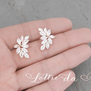 May include: A pair of gold earrings with a floral design featuring clear cubic zirconia stones.