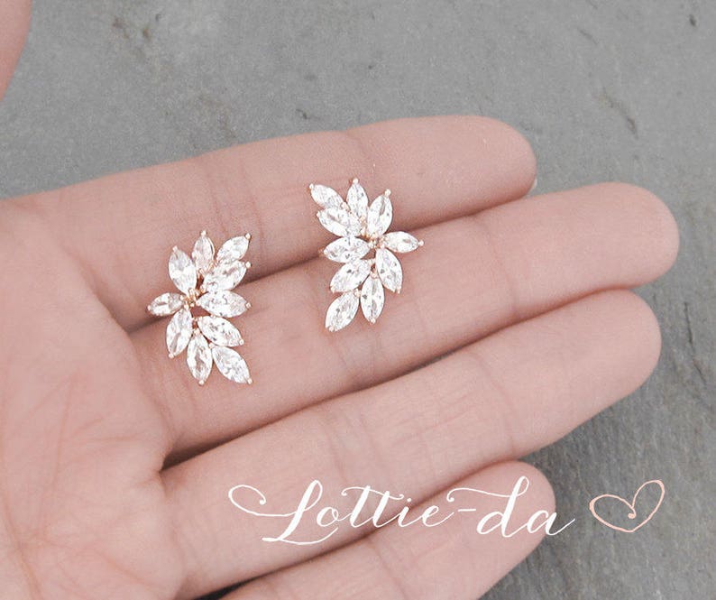 May include: A pair of gold earrings with a floral design featuring clear cubic zirconia stones.