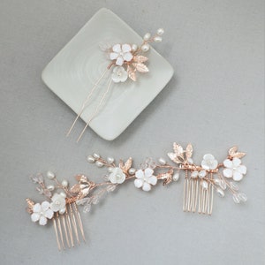 May include: Two hair combs with delicate floral designs. The combs feature white flowers, gold leaves, and pearl accents. The larger comb has a comb on one end and a floral design on the other. The smaller comb has a single floral design.