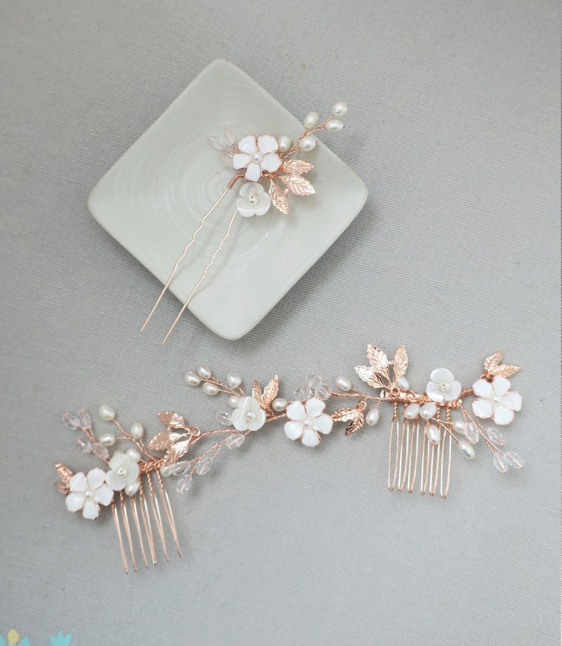 May include: Two hair combs with delicate floral designs. The combs feature white flowers, gold leaves, and pearl accents. The larger comb has a comb on one end and a floral design on the other. The smaller comb has a single floral design.