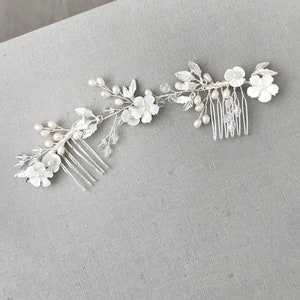 May include: Two silver hair combs with white pearl and flower accents. The combs are connected by a silver chain with white pearls and leaves.