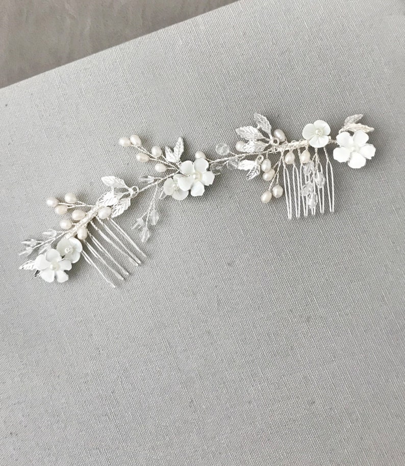 May include: Two silver hair combs with white pearl and flower accents. The combs are connected by a silver chain with white pearls and leaves.