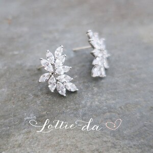 May include: A pair of silver earrings with a floral design featuring clear cubic zirconia stones.