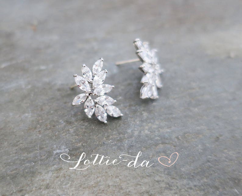 May include: A pair of silver earrings with a floral design featuring clear cubic zirconia stones.