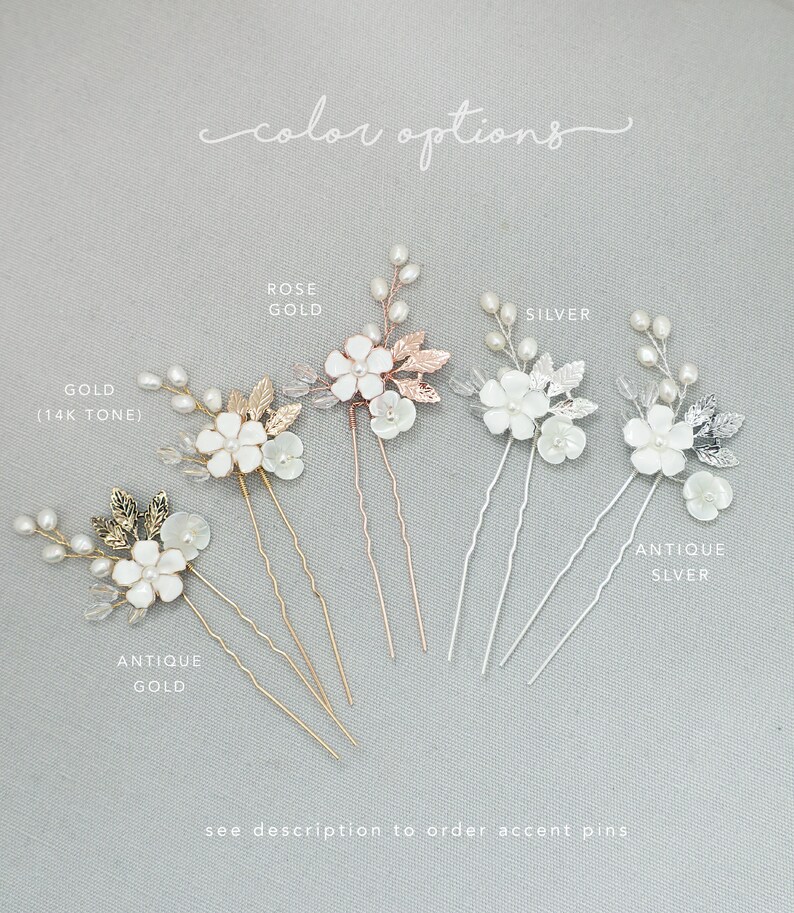 May include: Six hair pins with white pearl flowers and leaves in different metal finishes: antique gold, gold (14k tone), rose gold, silver, and antique silver. The text "color options" is written above the pins.