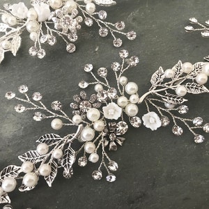 Pu&ograve; includere: Pettine per capelli argentato con decorazioni di perle bianche e cristalli a forma di fiori.