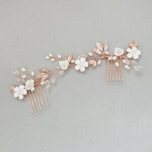 May include: Rose gold hair comb with white flowers and pearl accents. The comb has two rows of teeth and is designed to be worn in the hair.