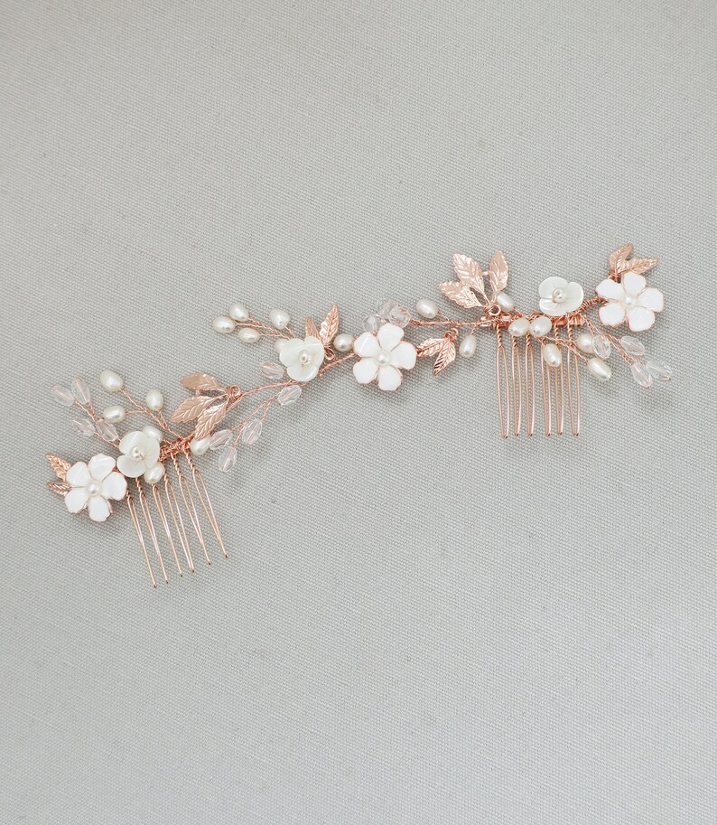 May include: Rose gold hair comb with white flowers and pearl accents. The comb has two rows of teeth and is designed to be worn in the hair.