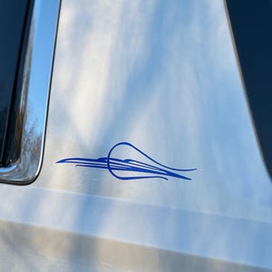 Puede incluir: Una calcomanía azul de raya fina en un vehículo plateado. La calcomanía presenta un diseño estilizado con líneas curvas y una forma de lágrima. Se ven la ventana y el embellecedor del vehículo.