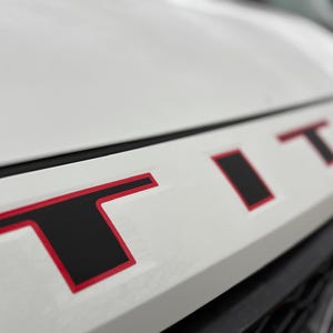 May include: White truck hood with a black and red "TITAN" emblem.