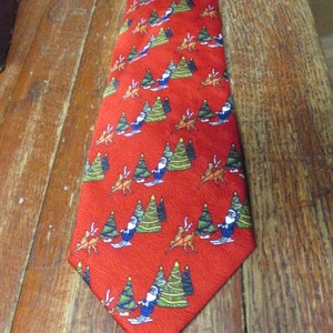 May include: Red Christmas tie with a repeating pattern of Santa Claus skiing, Christmas trees, and reindeer. The tie is made of a shiny fabric and is suitable for the holiday season.
